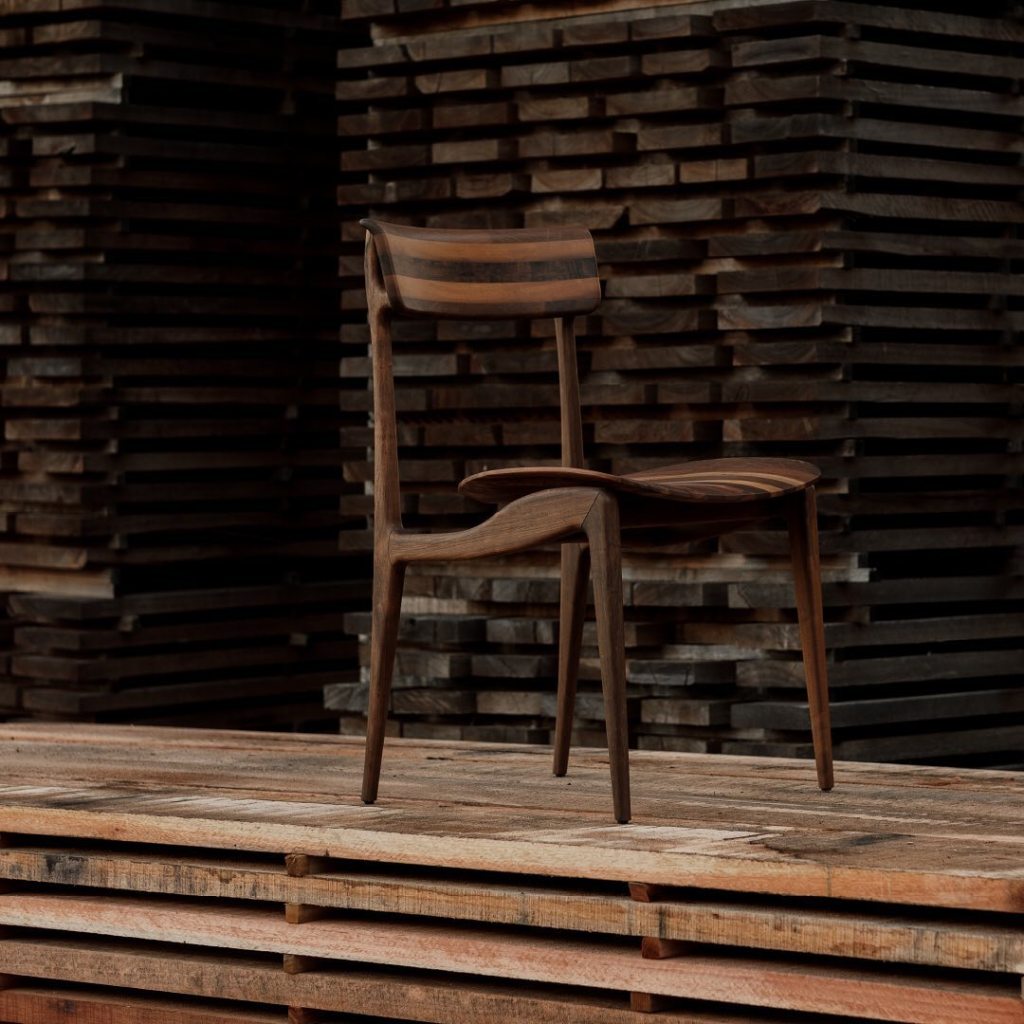 Elegant wooden chair crafted from certified Brazilian hardwood, photographed in front of stacked wood planks at a furniture workshop