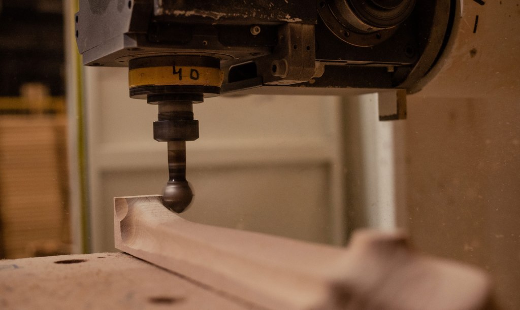 Close-up of CNC woodworking machine shaping solid wood furniture part in a Brazilian factory.