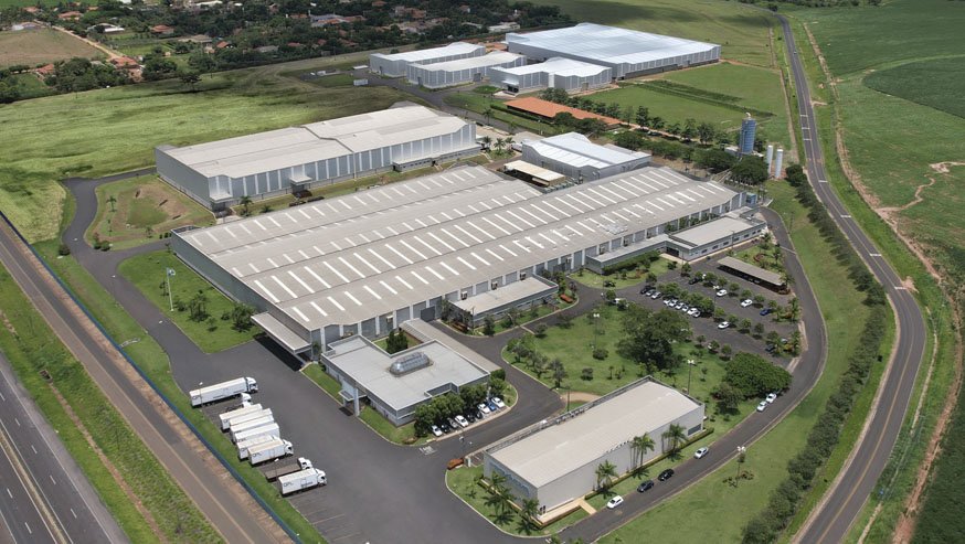 Aerial view of a large-scale furniture manufacturing facility in Brazil, surrounded by green fields and connected to logistics infrastructure.
