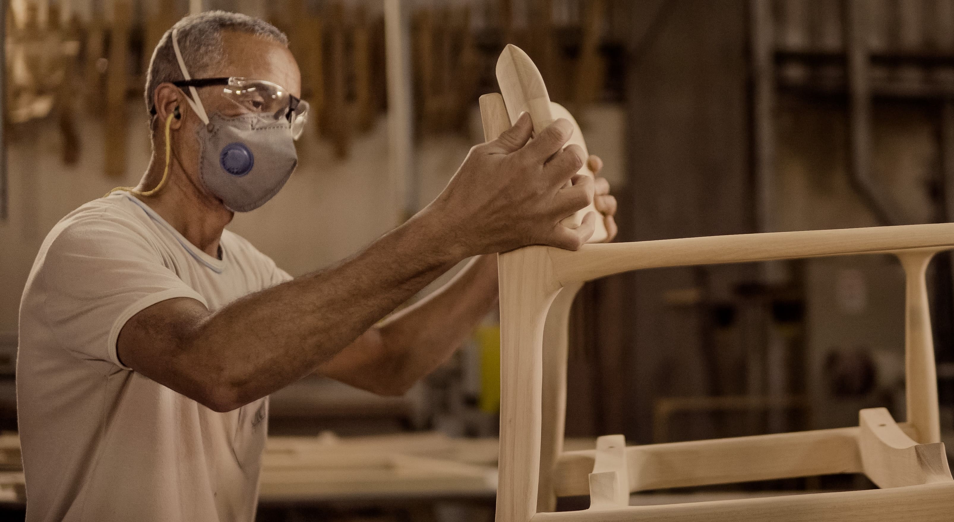 Brazilian craftsman working on a wooden chair frame in a furniture factory
