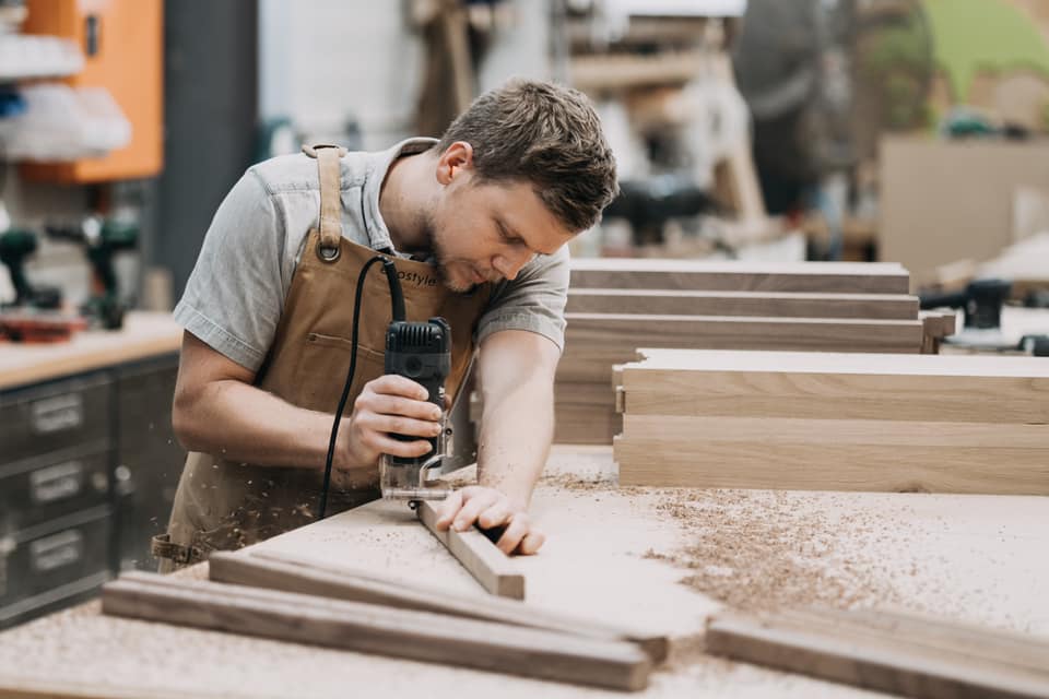 Brazilian woodworker using CNC router to craft solid wood components in a modern furniture factory