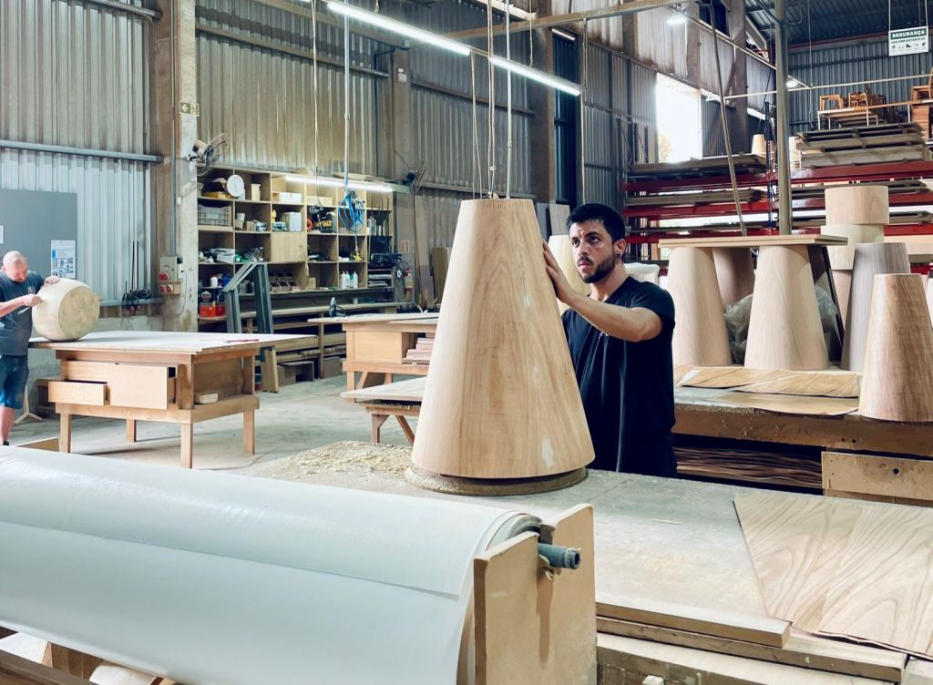 Brazilian furniture manufacturing workshop with craftsman shaping wooden furniture components.